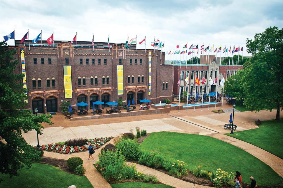 Photo of the Center for Global Citizenship, a large brick building with a number of flags flying from the roof. It is a sunny day with a view of the surrounding path and greenery.