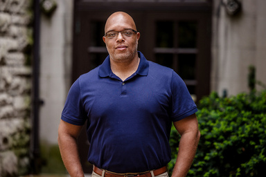 Image of Courtney Everett, a Black man with a shaved head and glasses, wearing a navy blue polo shirt.