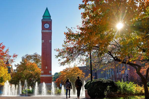 Pictured is SLU's Clock Tower and surrounding fountains spraying water as two students walk by in the fall weather. 