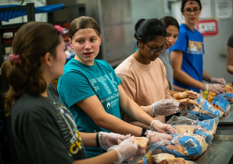 Image of a multicultural group of students, wearing latex gloves and working on food preparation for the student organization Campus Kitchen.